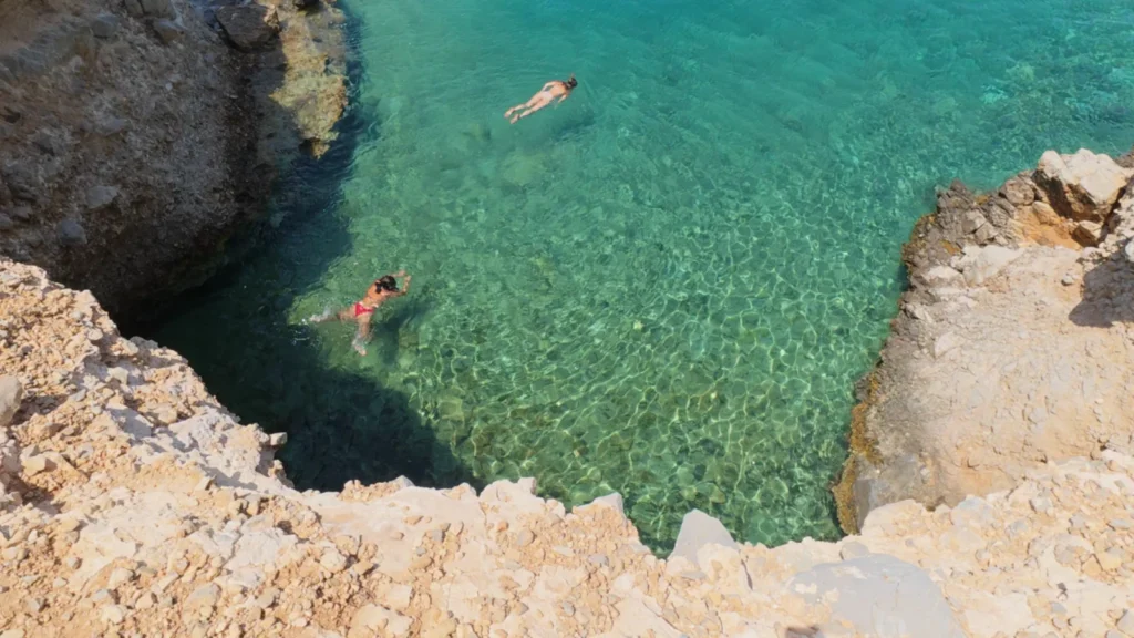 Swimmers snorkelling in a clear rocky cove on Moni island