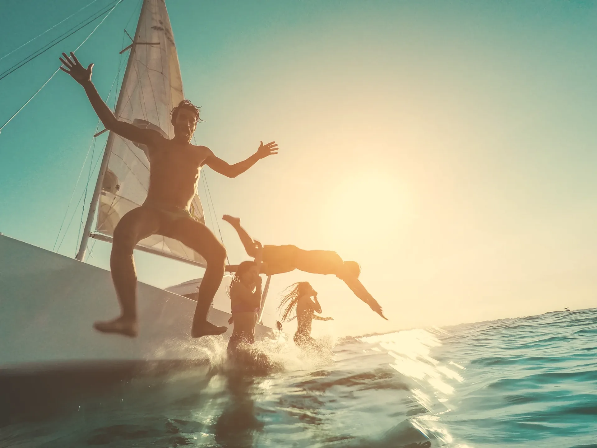 Friends jumping into the sea from a sailboat