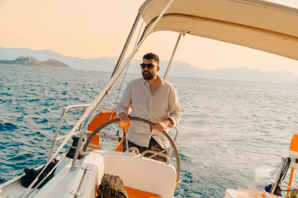 Sailing at the helm of a yacht in the late afternoon light, islands behind