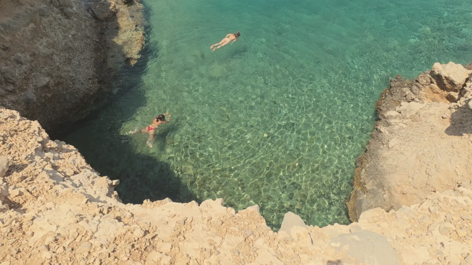 Swimmers snorkelling in a clear rocky cove on Moni island